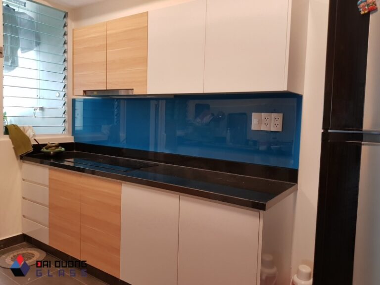 Kính ốp bếp màu xanh dương đậm, mặt đá đen, tủ gỗ màu sáng