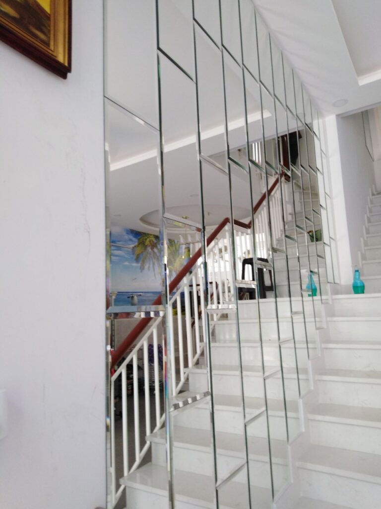 Bảng Báo Giá Thi Công Kính Thủy Trang Trí Trọn Gói Tại TP.HCM (Cập Nhật 2026) 15 Tường cầu thang ốp kính thủy dạng nan dọc chạy theo bậc thang màu trắng